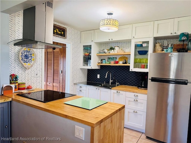 kitchen with stainless steel fridge, butcher block countertops, wall chimney exhaust hood, and black electric cooktop