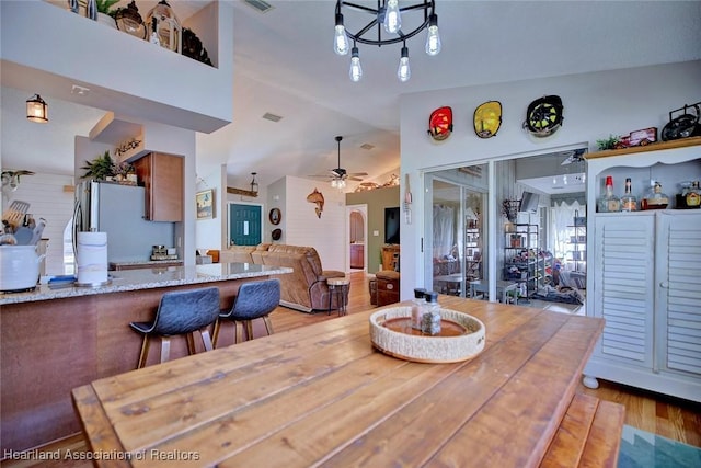 dining space with wood-type flooring, vaulted ceiling, and ceiling fan with notable chandelier