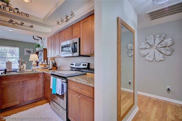 kitchen featuring a raised ceiling, sink, light stone counters, stainless steel appliances, and light hardwood / wood-style flooring