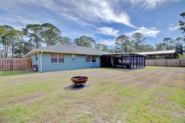 rear view of property featuring a sunroom, a yard, and a fire pit