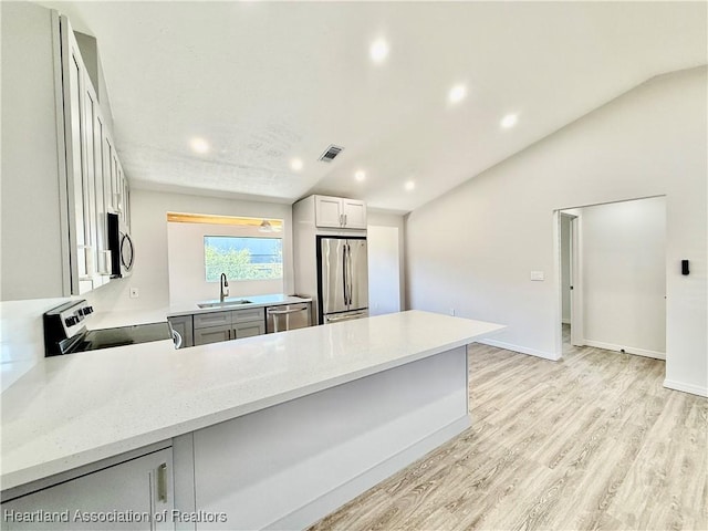 kitchen featuring vaulted ceiling, sink, kitchen peninsula, stainless steel appliances, and light hardwood / wood-style flooring