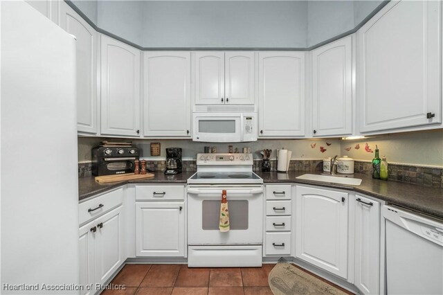 kitchen featuring white appliances, white cabinetry, dark countertops, and dark tile patterned floors