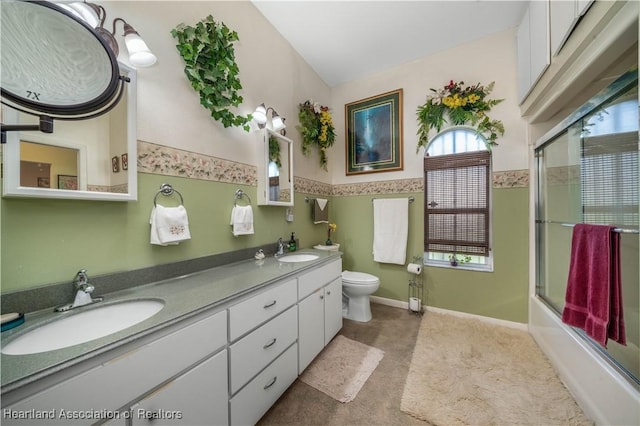 full bath featuring a sink, shower / bath combination with glass door, toilet, and double vanity