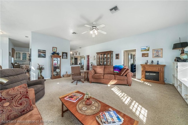 carpeted living room featuring visible vents, a glass covered fireplace, and ceiling fan