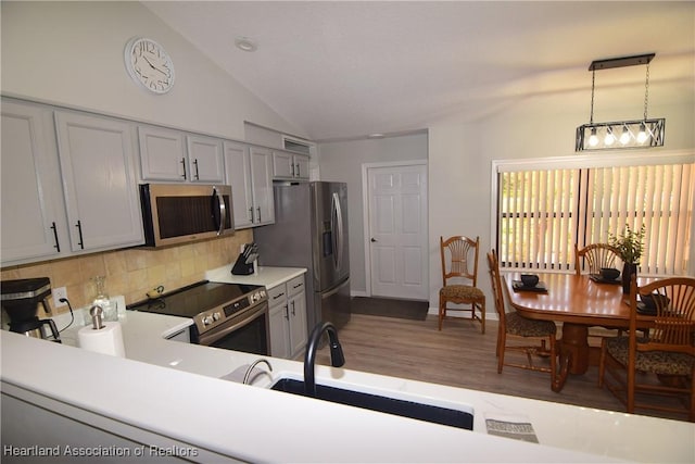 kitchen with sink, hanging light fixtures, vaulted ceiling, decorative backsplash, and appliances with stainless steel finishes