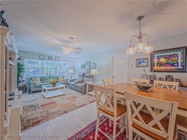 dining room featuring a textured ceiling, visible vents, ceiling fan, and wood finished floors