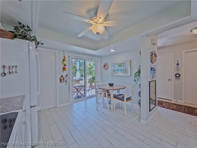 dining area featuring baseboards, a raised ceiling, and ceiling fan