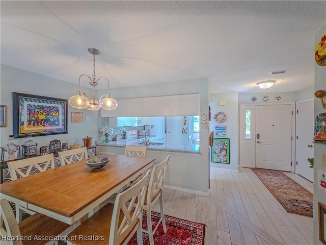 dining room with baseboards, visible vents, a textured ceiling, and light wood-style flooring