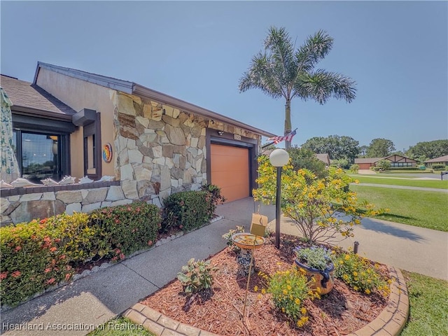 exterior space featuring a garage, a yard, concrete driveway, and stone siding