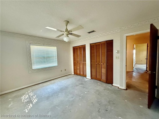 unfurnished bedroom with a textured ceiling, concrete floors, two closets, baseboards, and visible vents