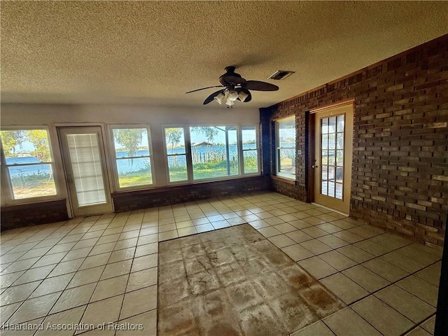 unfurnished sunroom featuring a textured ceiling, tile patterned flooring, brick wall, and visible vents