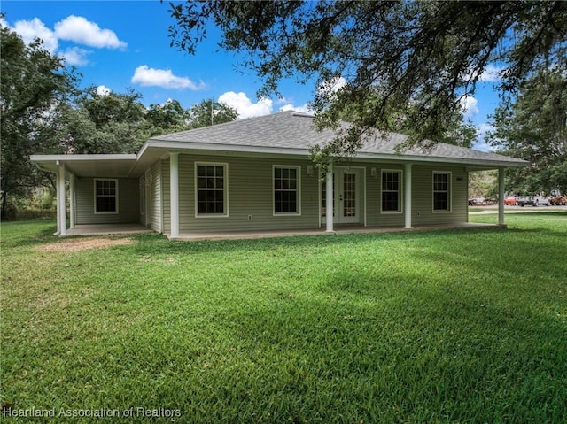back of property featuring a yard, an attached carport, a patio area, and a shingled roof