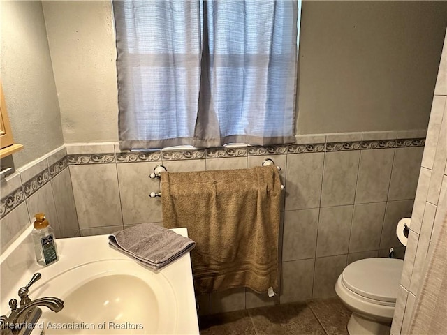 half bathroom featuring toilet, tile patterned flooring, tile walls, and a sink