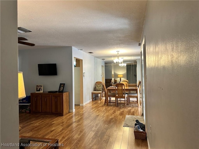 dining area with visible vents, a textured ceiling, wood finished floors, baseboards, and ceiling fan with notable chandelier