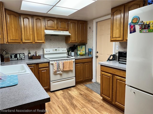 kitchen with white appliances, light wood finished floors, brown cabinetry, under cabinet range hood, and a sink