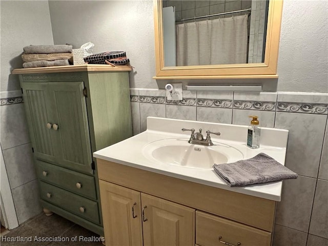 bathroom featuring a shower with shower curtain, wainscoting, tile walls, and vanity