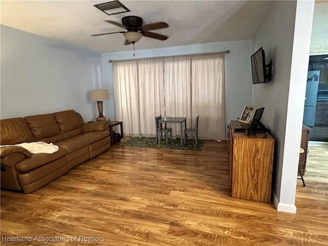 living area with ceiling fan, a textured ceiling, and wood finished floors