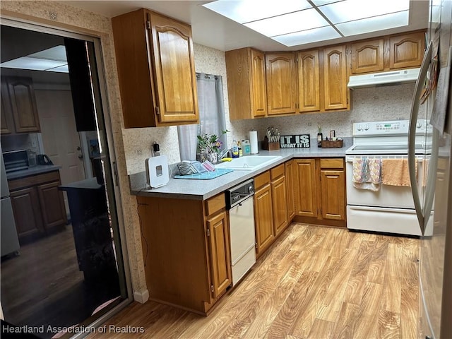 kitchen with light wood-style flooring, under cabinet range hood, white appliances, a sink, and brown cabinets