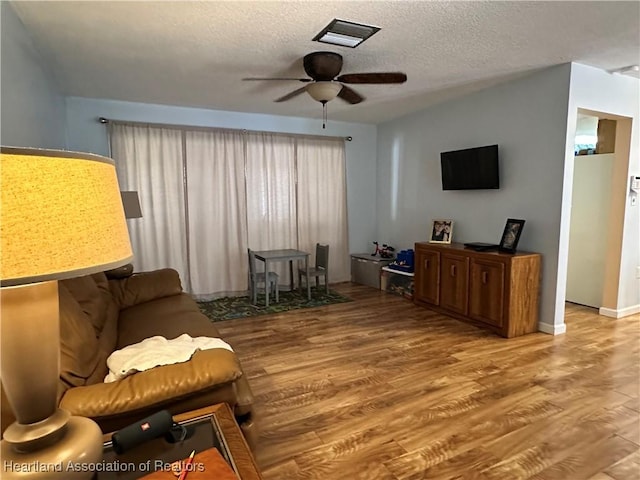 living area with ceiling fan, a textured ceiling, and wood finished floors