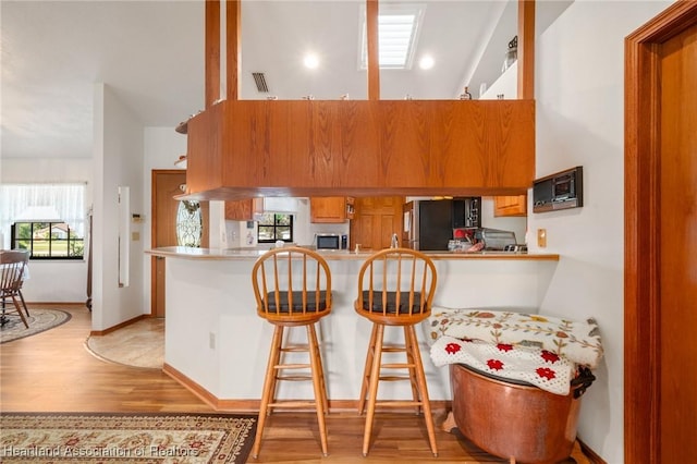 kitchen with stainless steel appliances, a kitchen bar, kitchen peninsula, and light wood-type flooring