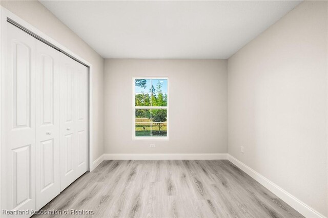 unfurnished bedroom featuring baseboards, light wood finished floors, and a closet