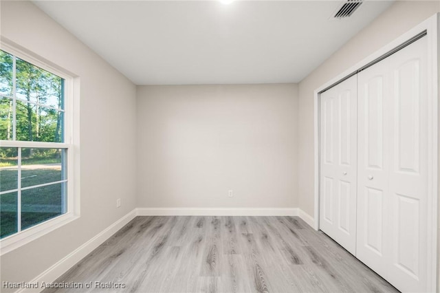 unfurnished bedroom with a closet, light wood finished floors, baseboards, and visible vents