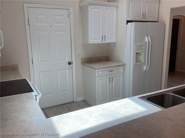 kitchen with white appliances, white cabinetry, arched walkways, a sink, and light tile patterned floors