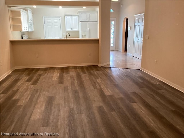 unfurnished living room featuring arched walkways, baseboards, and dark wood-type flooring