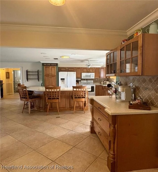 kitchen featuring white appliances, a kitchen bar, decorative backsplash, light tile patterned floors, and ornamental molding