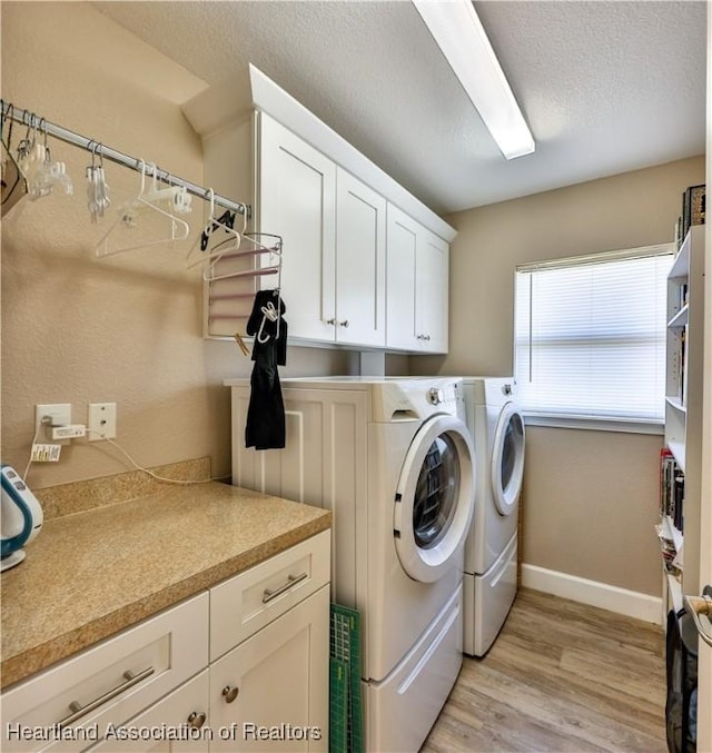 laundry room with washing machine and clothes dryer, cabinets, a textured ceiling, and light hardwood / wood-style floors