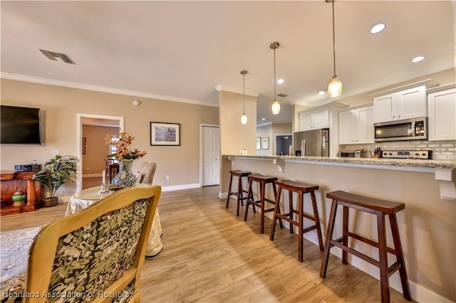 kitchen featuring white cabinets, hanging light fixtures, light stone countertops, appliances with stainless steel finishes, and a breakfast bar area