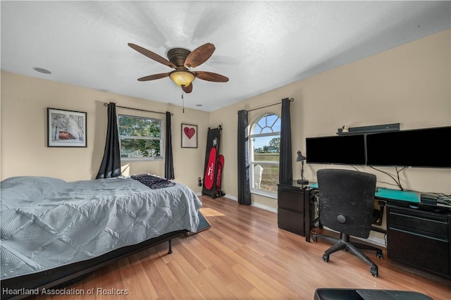 bedroom featuring baseboards, ceiling fan, wood finished floors, and multiple windows