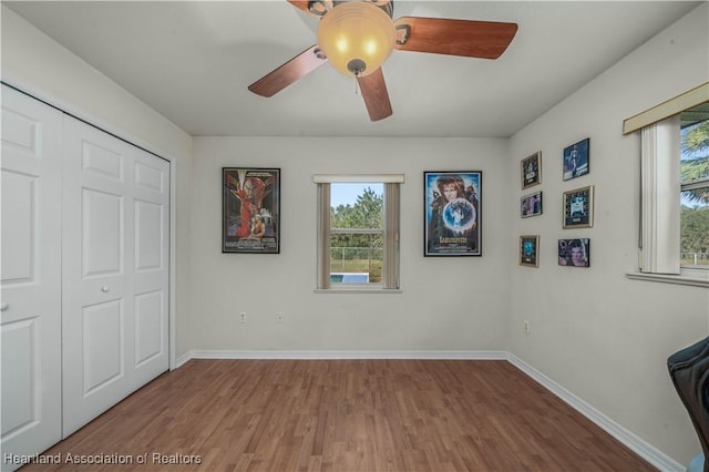 unfurnished bedroom with baseboards, wood finished floors, a closet, and a ceiling fan
