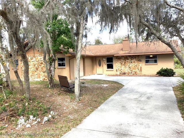 single story home featuring stone siding, driveway, a chimney, and stucco siding