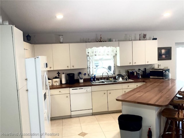 kitchen featuring light tile patterned floors, wooden counters, a sink, white appliances, and a peninsula