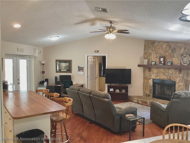 living room with vaulted ceiling, a fireplace, wood finished floors, and visible vents