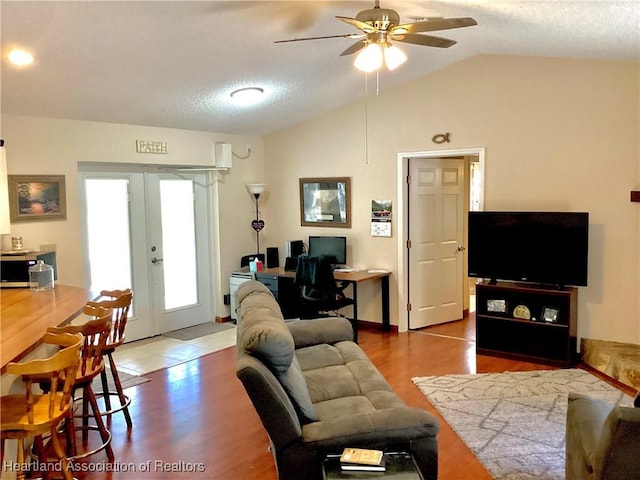 living area with ceiling fan, wood finished floors, vaulted ceiling, a textured ceiling, and french doors