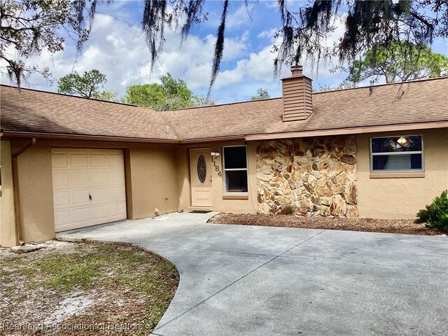 entrance to property with driveway, stone siding, an attached garage, and a shingled roof