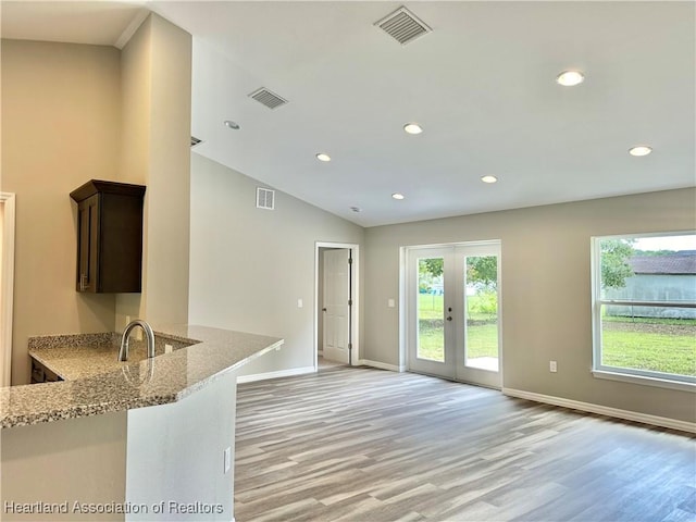 kitchen featuring sink, light stone counters, kitchen peninsula, light hardwood / wood-style floors, and lofted ceiling