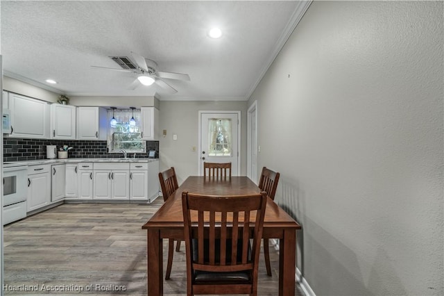 dining room featuring ceiling fan, sink, light hardwood / wood-style floors, a textured ceiling, and ornamental molding