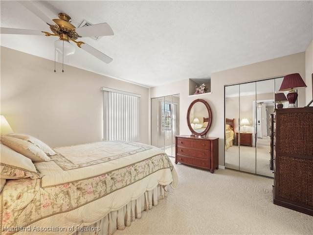 bedroom with ceiling fan, a textured ceiling, light carpet, and two closets