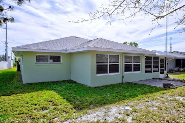 back of property with roof with shingles, stucco siding, a lawn, a sunroom, and a patio area