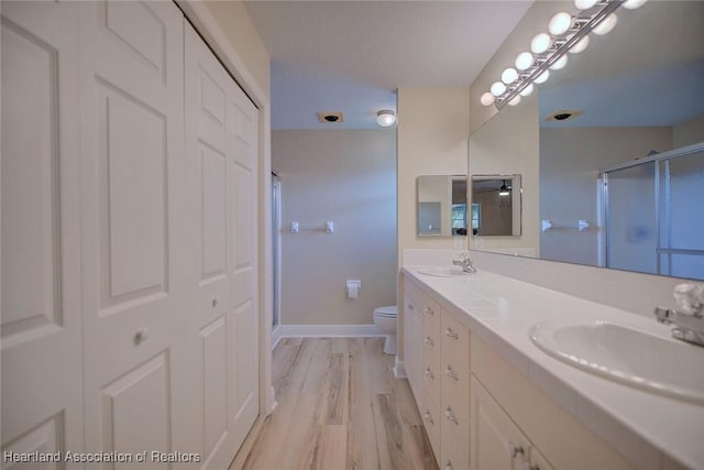 full bathroom featuring a stall shower, a sink, toilet, and wood finished floors