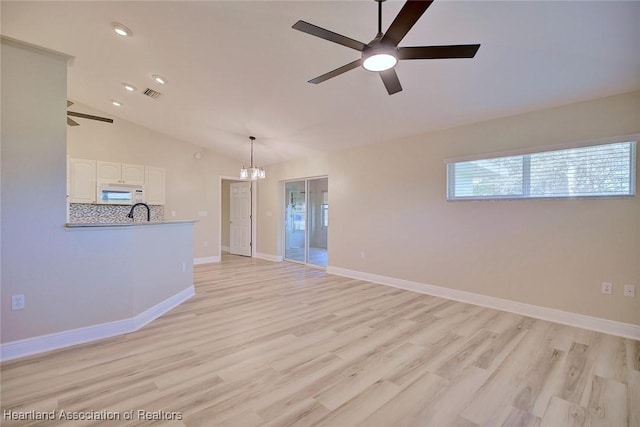 spare room featuring vaulted ceiling, ceiling fan with notable chandelier, baseboards, and light wood-style floors