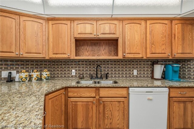 kitchen with decorative backsplash, white dishwasher, light stone countertops, and sink