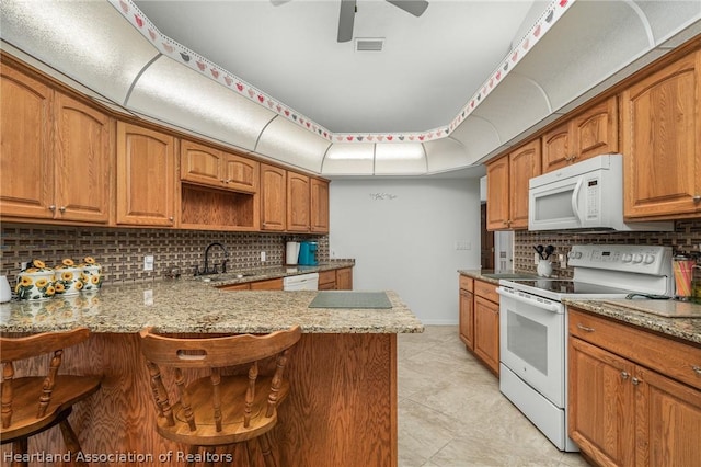 kitchen featuring kitchen peninsula, light stone counters, white appliances, ceiling fan, and sink