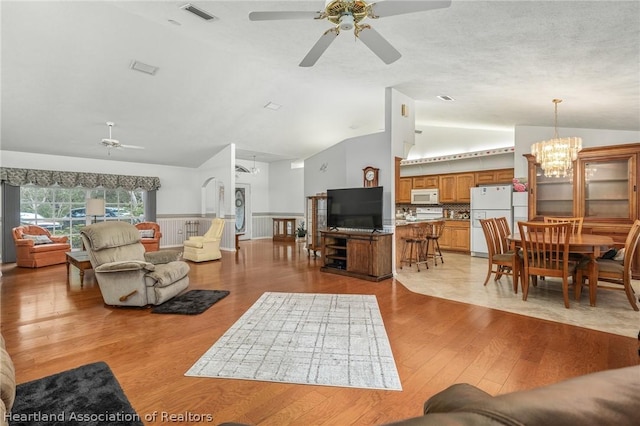 living room with ceiling fan with notable chandelier, lofted ceiling, and light hardwood / wood-style flooring