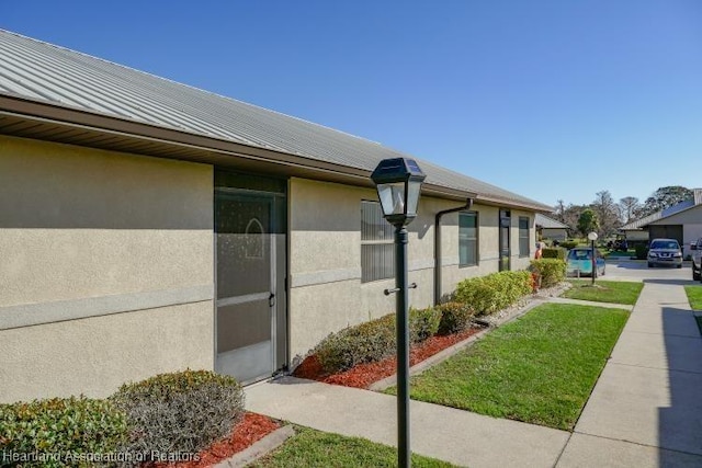 view of side of home with a standing seam roof, metal roof, a lawn, and stucco siding