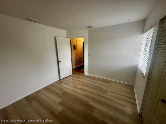 unfurnished bedroom with baseboards, wood finished floors, and visible vents