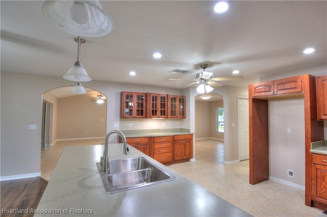 kitchen featuring visible vents, a sink, arched walkways, glass insert cabinets, and ceiling fan